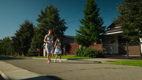 woman in floral dress runs alongside visibly tired little girl on quiet residential estate street, holding hands as they move quickly under clear blue sky surrounded by trees, fences, and private homes