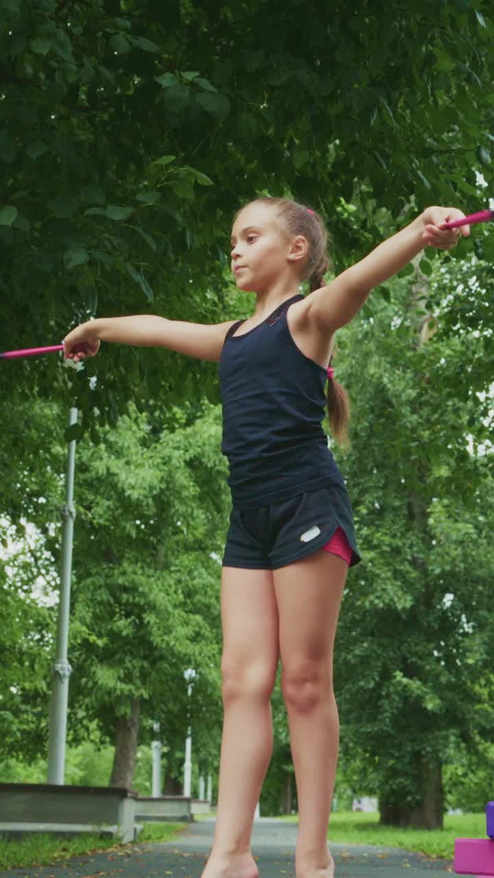 A Young Performer Showcases Balance and Coordination While Practicing with Rhythm Sticks in a Lush Outdoor Environment, Exemplifying Grace and Focus in Motion