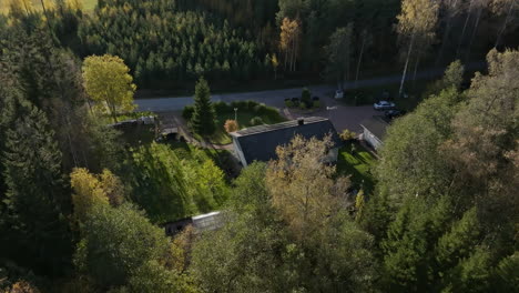 Drone-shot-over-forest,-revealing-a-house-with-sunlight-collectors,-autumn-day