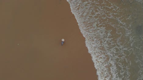 4k-Aerial-Top-Down-Tracking-shot-of-a-Beautiful-27-year-old-Indian-woman-walking-by-the-shore-enjoying-her-holidays-in-pretty-serene-Varkala-wearing-white-and-Blue-tops-with-a-Big-Hat-on-her-head