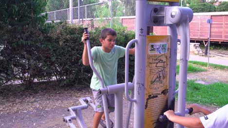 imágenes de dos niños caucásicos haciendo ejercicio al aire libre, en equipos de gimnasia de parques públicos