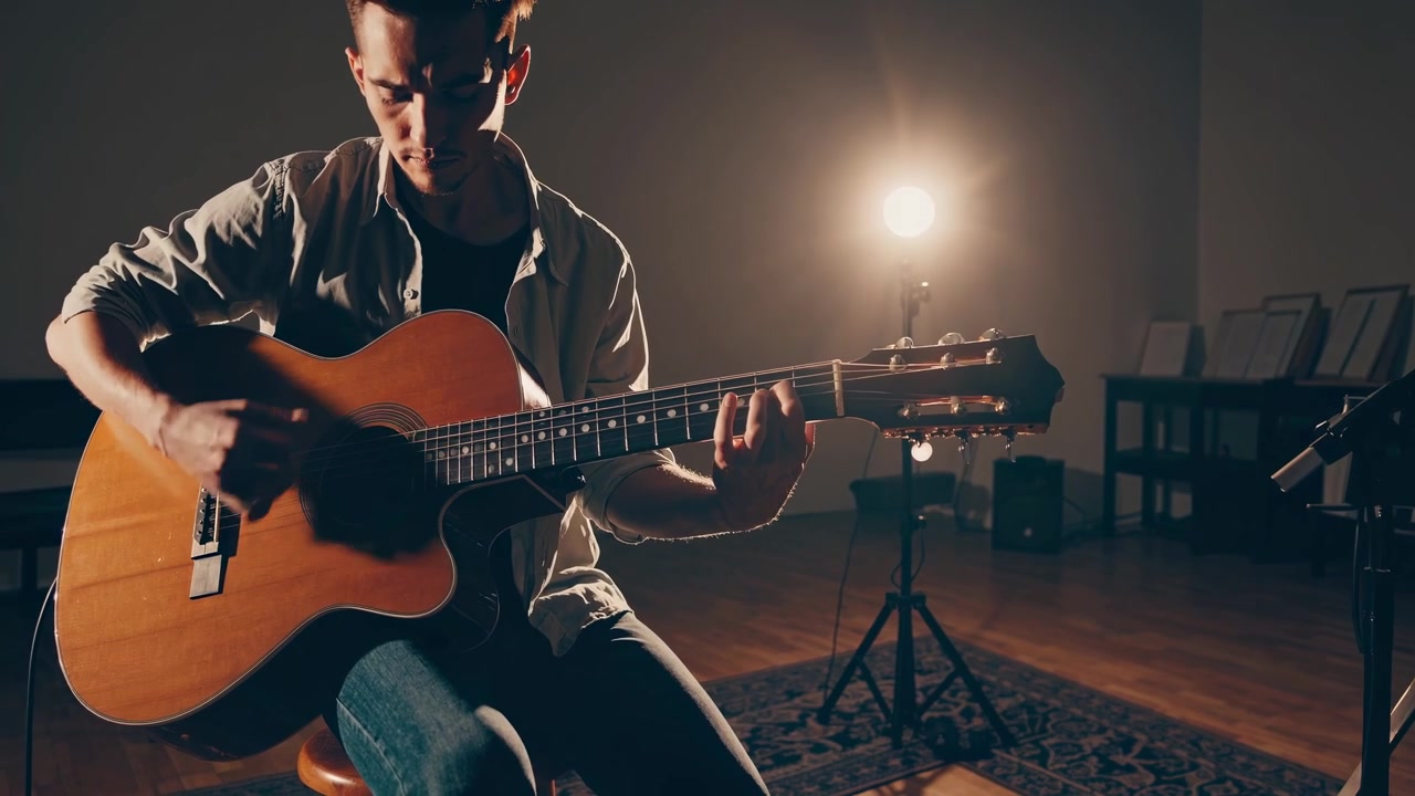 Giovane uomo che suona la chitarra acustica in uno studio in penombra