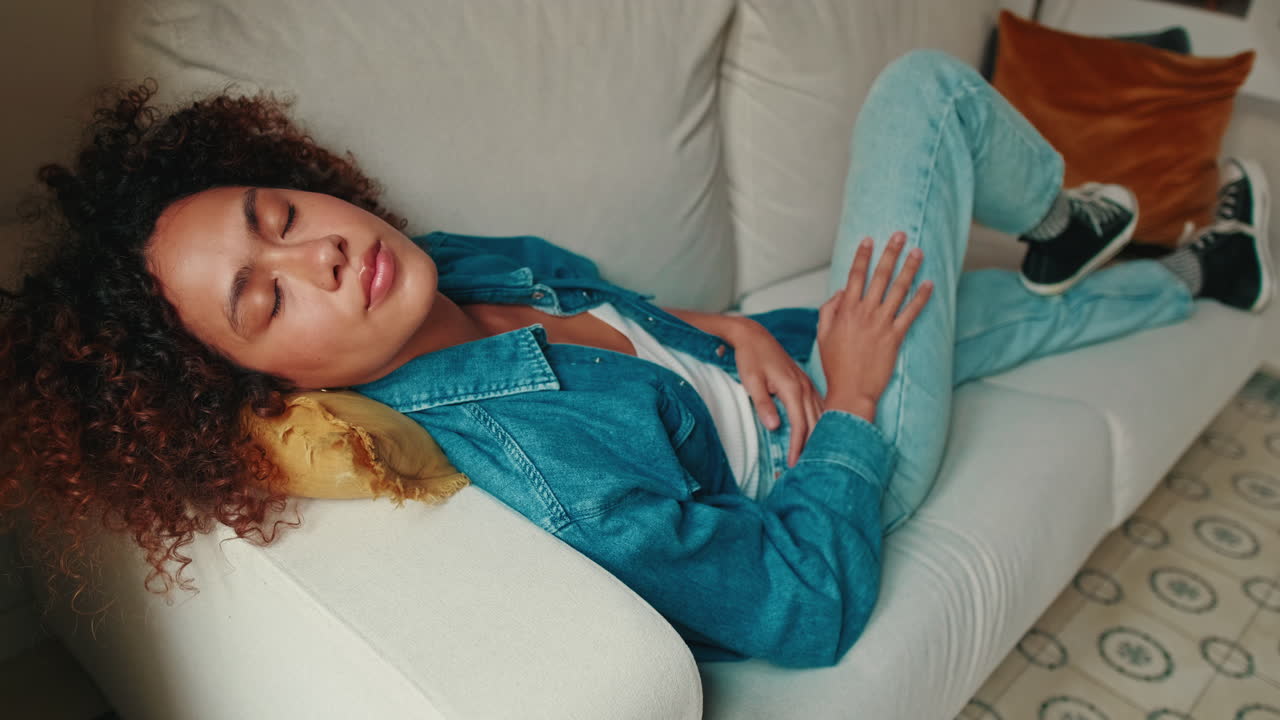 Peaceful Young Woman with Curly Hair Resting on Sofa