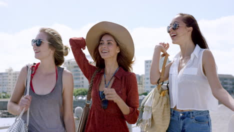 Three-young-women-tourists-on-summer-vacation-girl-friends-walking-on-beach-promenade