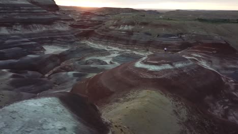 Orbit-Luftbild-Eines-Mannes,-Der-Auf-Sandsteinhügeln-Mit-Farbigen-Schichten-Steht,-Wüste-Von-Utah,-Hanksville,-USA
