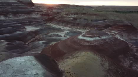 orbit aerial view of male standing on top of sandstone hills with colored layers, utah desert, hanksville usa