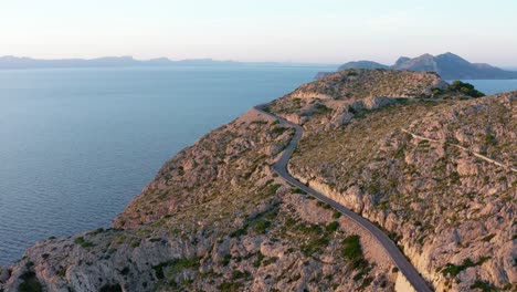 winding road on the edge of a cliff with a view of the blue ocean in a mountain landscape in orange light, aerial drone