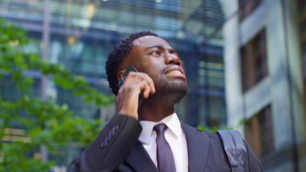 Young Businessman Wearing Suit Talking On Mobile Phone Walking Outside Offices In The Financial District Of The City Of London UK Shot In Rael Time