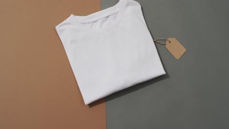 Video-of-flat-lay-of-folded-white-t-shirt-with-tag-and-copy-space-on-grey-and-brown-background