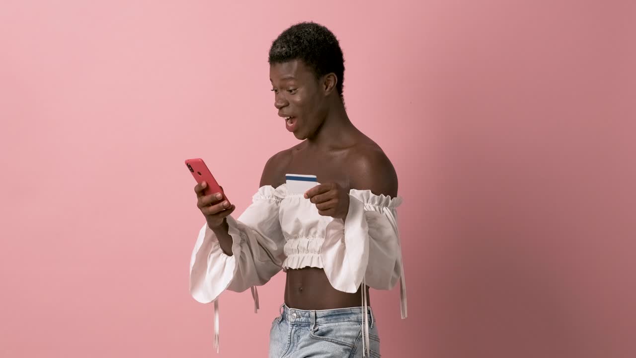 Afrikansk transperson smiler, mens vedkommende bruger mobiltelefon og kreditkort
