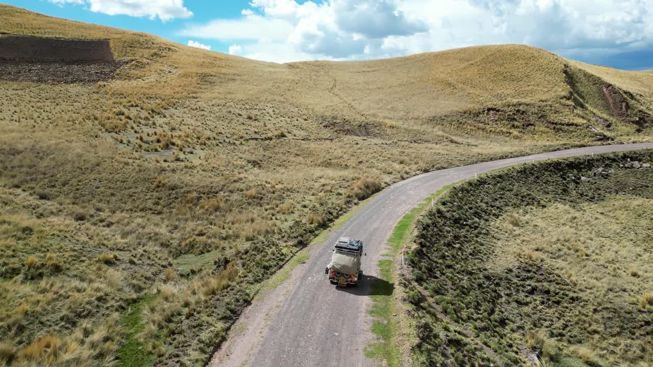 Aerial footage of a tuk tuk following a dirt path through endless grassy hills in the Andes, symbolizing freedom and solitude