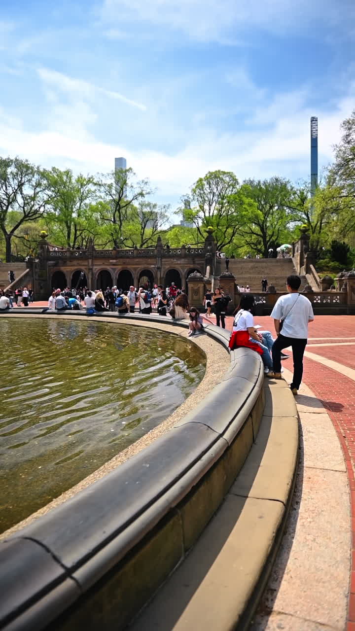 New York, USA, 1 agosto 2025: Bethesda Fountain and Terrace che si riflettono nel laghetto di Central Park. Visitatori seduti che camminano attorno all'acqua mentre gli archi storici si ergono sullo sfondo.