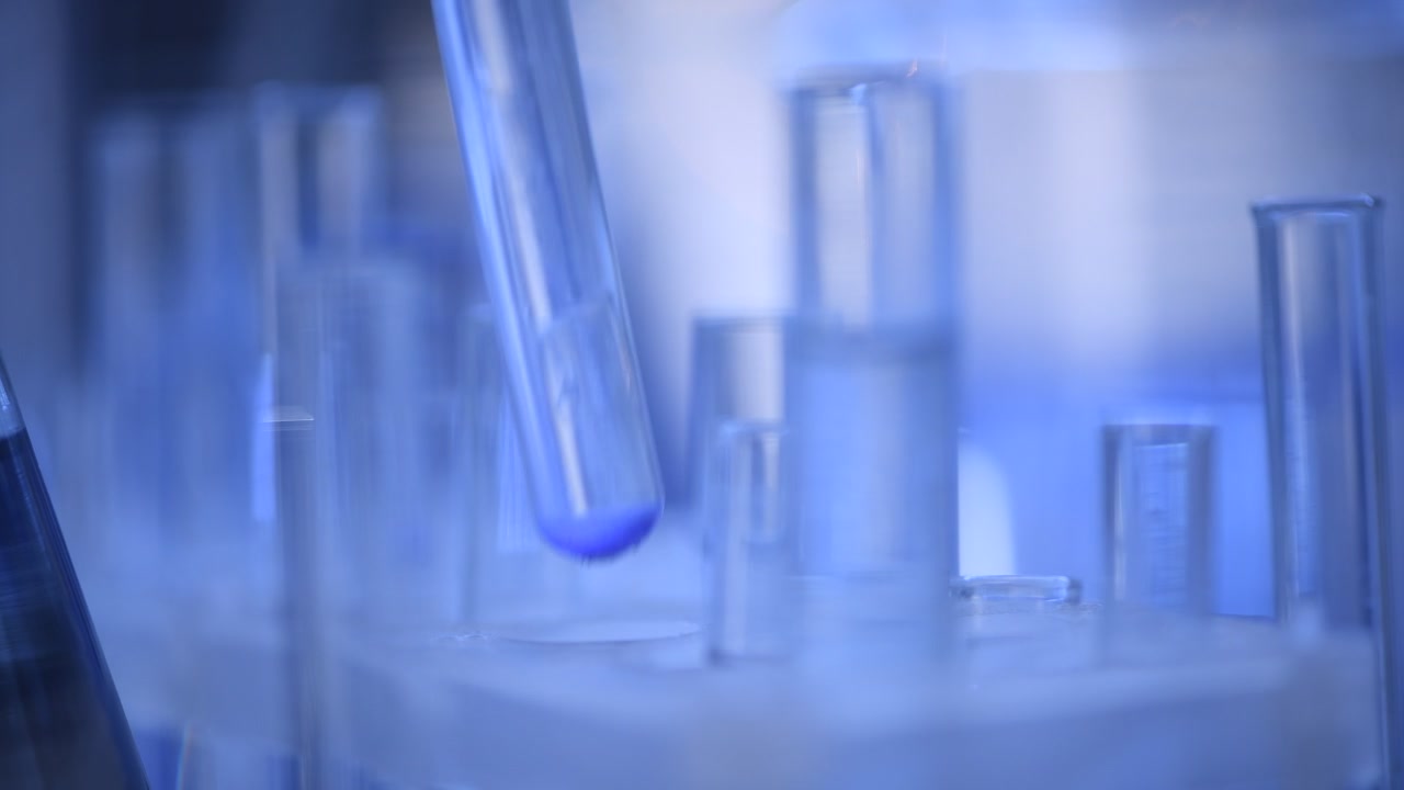 Gloved Hand Placing Test Tube with Blue Liquid in Laboratory Rack