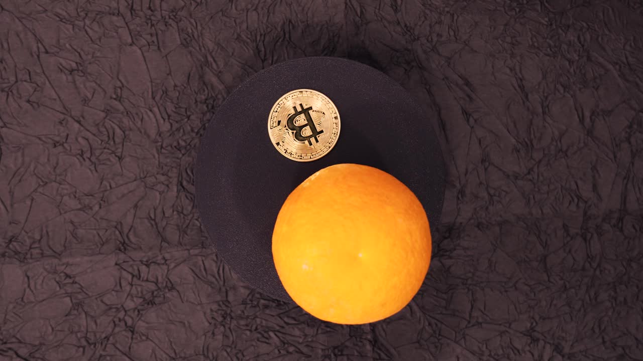 Bitcoin and orange balanced on black surface showcasing contrast between digital currency and fruit