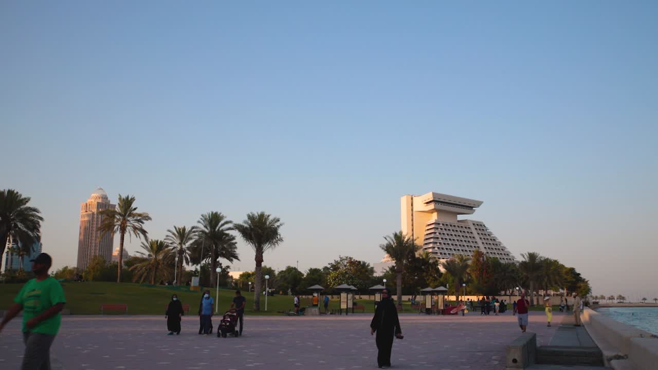 해가 지는 도하 코르니치 산책로에서 앉아있는 사람들, 고 있는 사람들, 배경에는 셰라톤 호텔이 보인다.