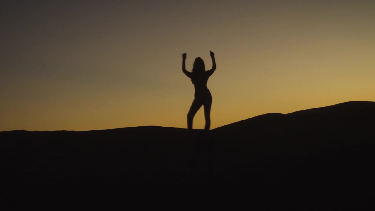 Silhouette di una donna nel deserto in piedi sulla cima di una duna al tramonto.