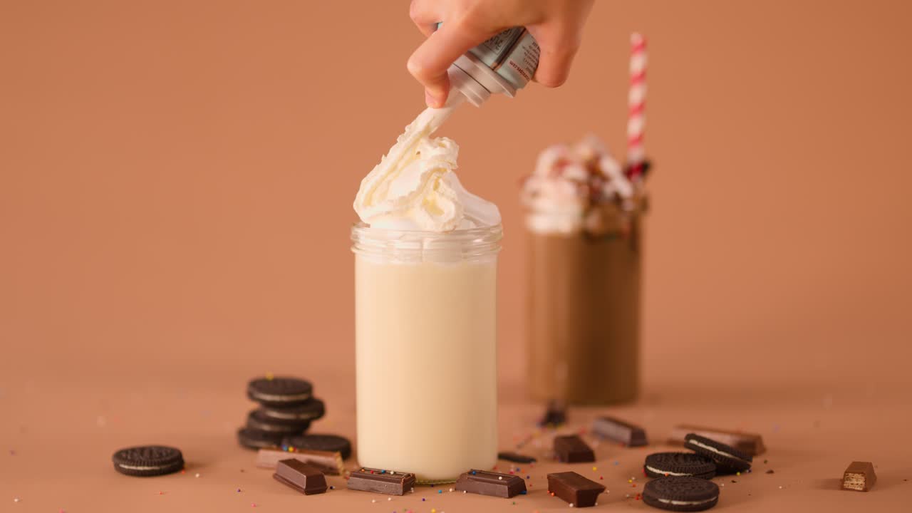 Close-up of hand sprinkling chocolate onto whipped cream vanilla milkshake, warm studio lighting