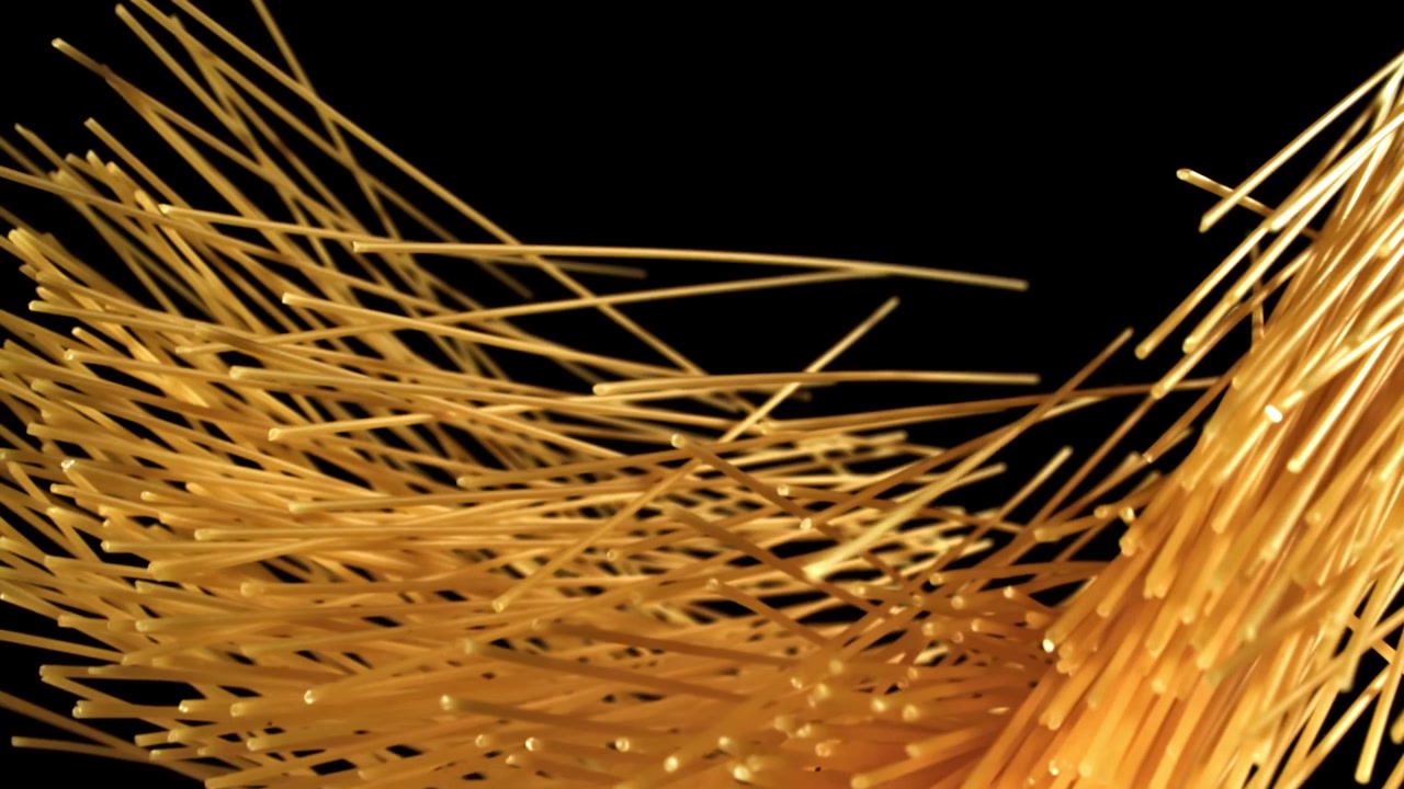 Spaghetti secchi che cadono e si disperdono su sfondo nero