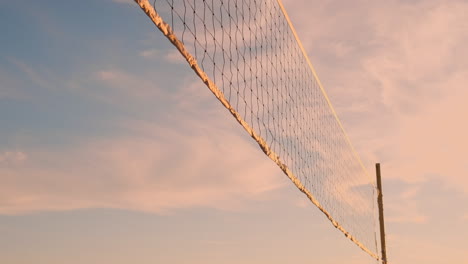 SLOW-MOTION-LOW-ANGLE-CLOSE-UP-SUN-FLARE:-Athletic-girl-playing-beach-volleyball-jumps-in-the-air-and-strikes-the-ball-over-the-net-on-a-beautiful-summer-evening.-Caucasian-woman-score-a-point.