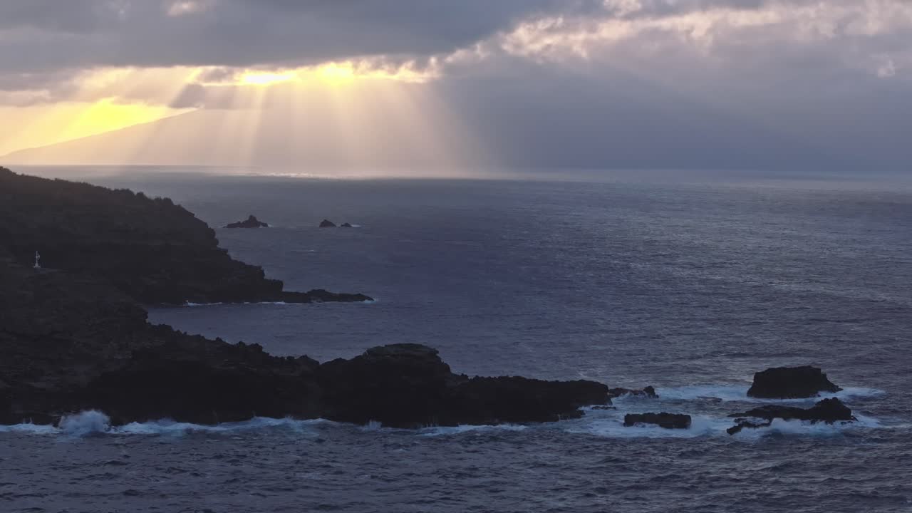 amplia vista aérea de las rocas dentadas y acantilados de maui al atardecer con el cielo nublado y los rayos de luz que irradian hacia el océano