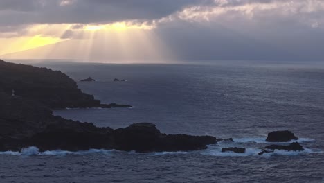 Weite-Luftaufnahme-Der-Schroffen-Felsen-Und-Klippen-Von-Maui-Bei-Sonnenuntergang-Mit-Bewölktem-Himmel-Und-Lichtstrahlen,-Die-Auf-Den-Ozean-Strahlen