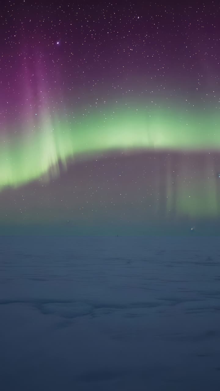 Vertical video: Shifting aurora forming green arc over ice plain, curtain growing as frames pass