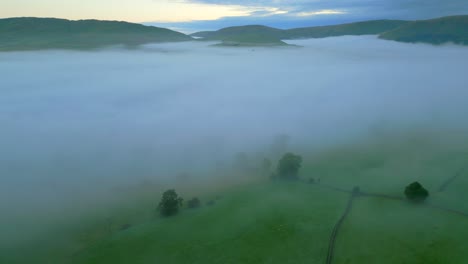 Volando-A-Lo-Largo-Del-Borde-Del-Banco-De-Niebla-Sobre-El-Campo-Con-Colinas-En-La-Distancia-Al-Amanecer