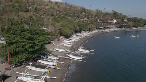 traditional outrigger canoes line pebble beach on bali, aerial flyover