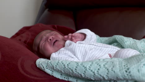 new born baby boy crying and fidgeting laying down on pillow on sofa