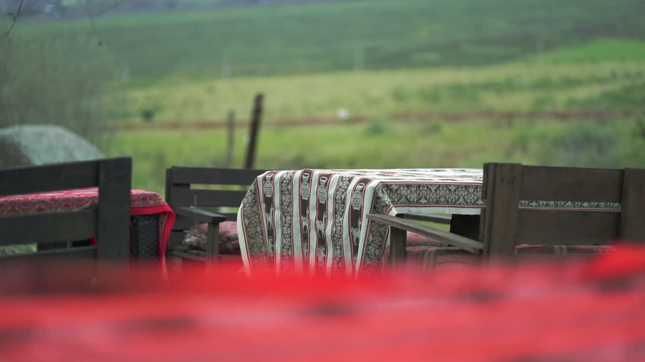 왼쪽에서 오른쪽으로 느리고 조용한 슬라이더 은 색과 패턴 옷을 가진 외부 목조 식탁과 배경에 흐릿한 녹색 시골 풍경