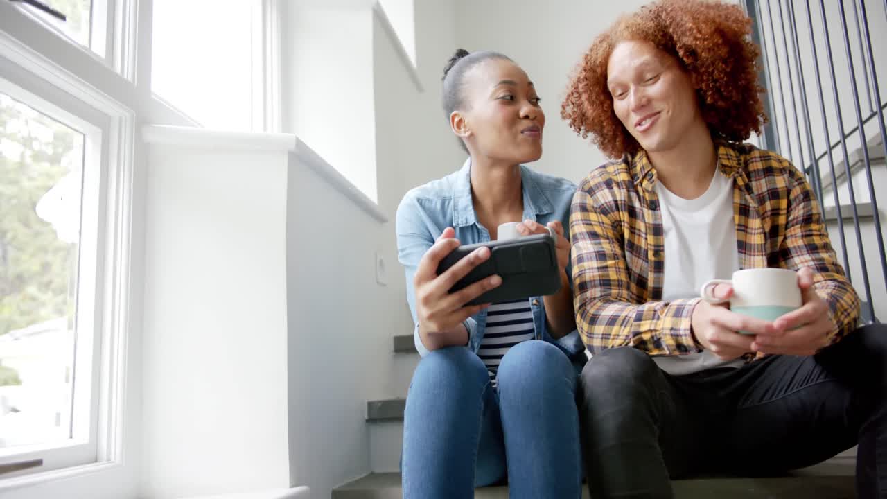 pareja feliz sentada en las escaleras, bebiendo café usando un teléfono inteligente y hablando, cámara lenta