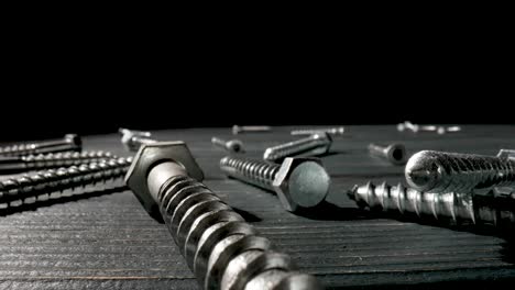 assortment of metal screws and bolts on a dark wooden surface