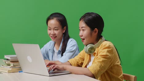 close up of asian woman students screaming goal celebrating succeed typing on a laptop while sitting on a table in the green screen background classroom