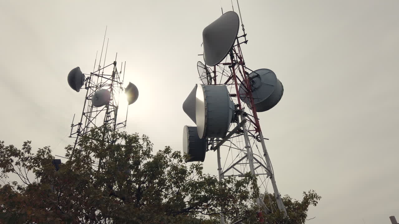 Low angle view of tall communication towers with antennas and dishes against cloudy sky