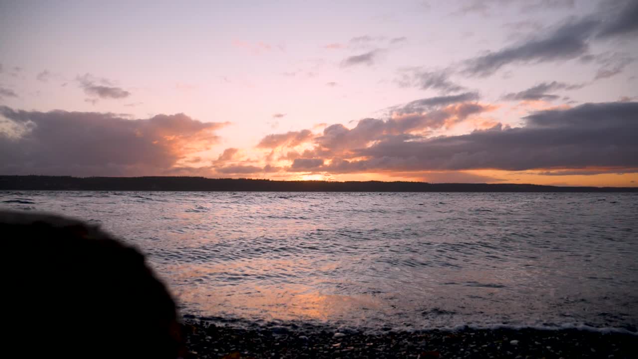 Reveal from behind a log of a sunset from Camano Island overlooking the Puget Sound.
