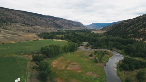 luftaufnahme dolly vorwärts über eine wunderschöne naturlandschaft in chance creek british columbia mit grünen feldern und einem fluss, der durch das tal in einem wüstental fließt