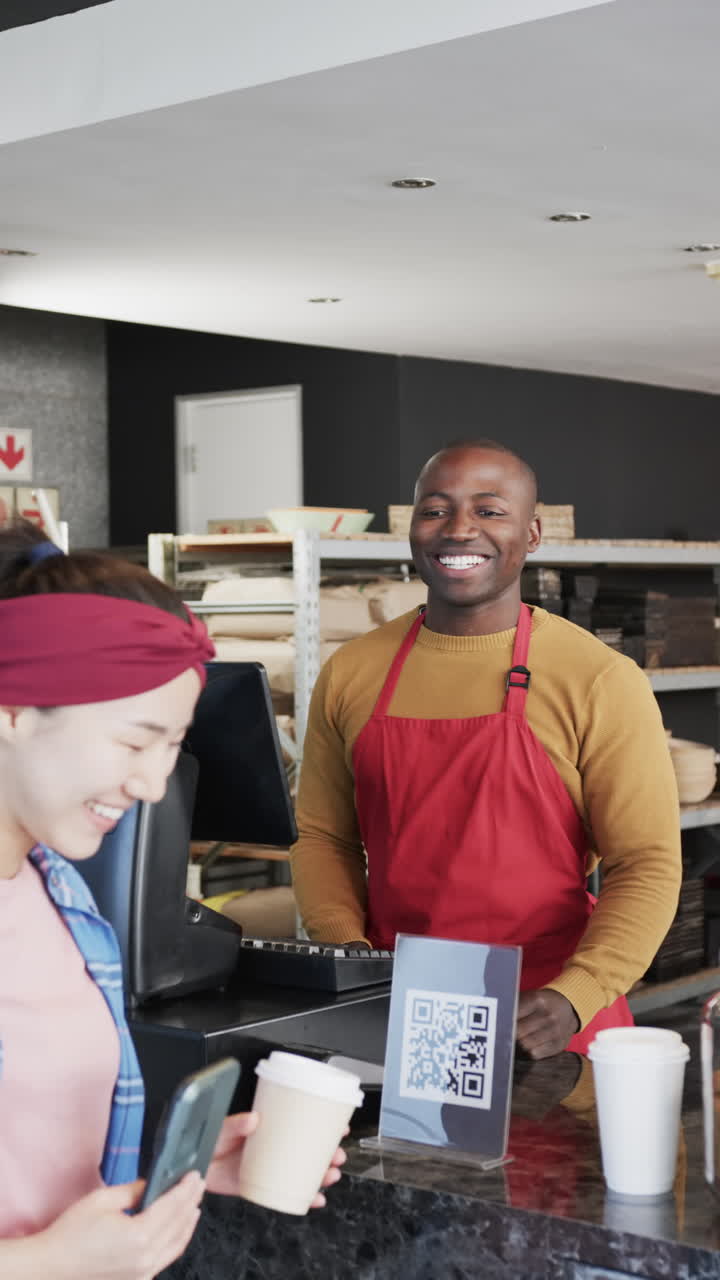 Vertical video of happy diverse worker and customer with coffee waving hands in slow motion