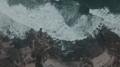 Aerial-top-down-view-of-ocean-waves-crashing-at-rocky-beach-at-day