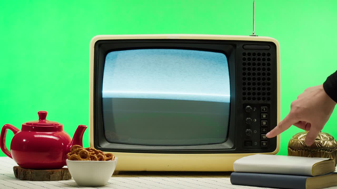 녹색 배경에 오래된 레트로 텔레비전의 클로즈업, 버튼을 누르기, 회색 간섭 스크린과 안테나, 주방 테이블에 빨간 차병, 나쁜 신호 수신, 촬영 개념