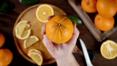 male hand puts a juicy orange on a cutting board.