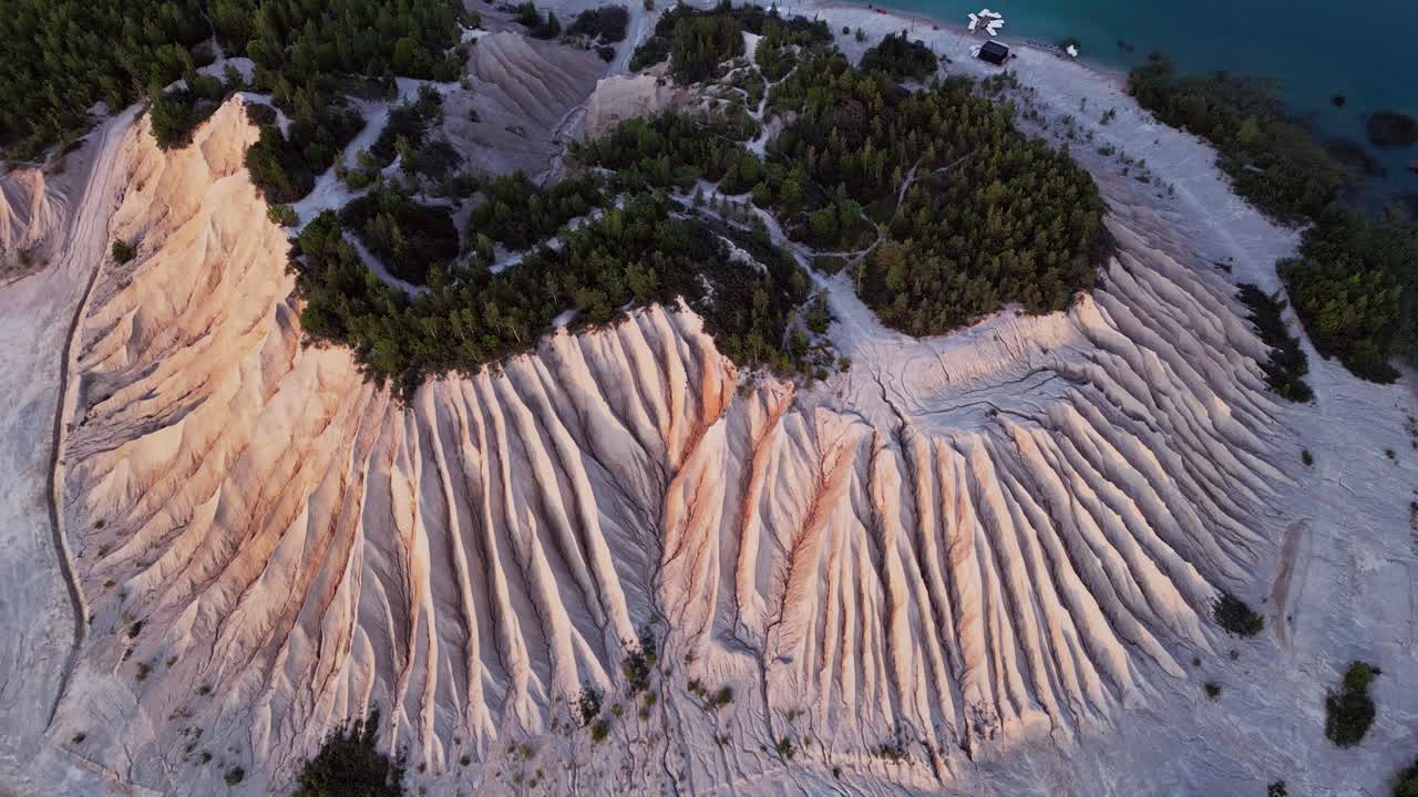 Rummu Quarry in Estonia filmed by drone reveals the massive white ash hill next to a flooded quarry with clear blue waters and old ruins surrounded by lush green trees