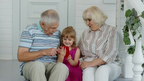 Senior-couple-sitting-with-granddaughter-and-using-mobile-phone-in-porch-at-home.-Online-shopping