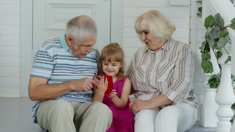 senior couple sitting with granddaughter and using mobile phone in porch at home. online shopping