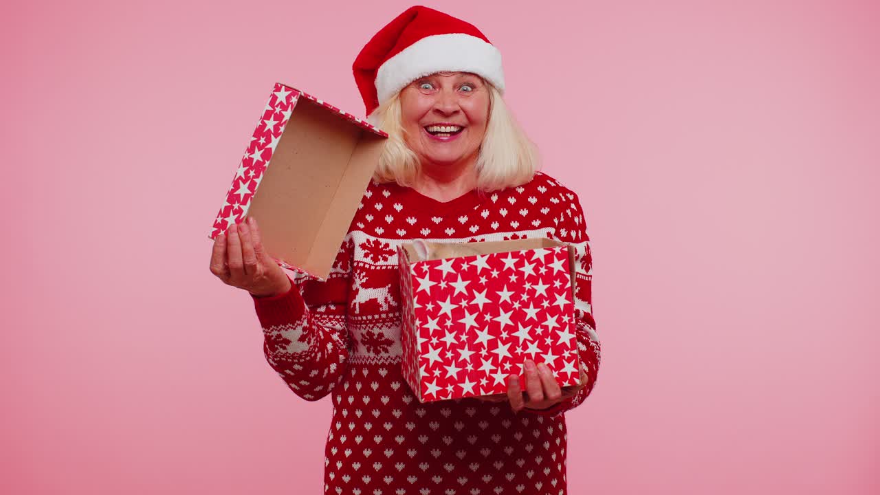 Grandmother in christmas sweater smiling unwrapping gift opening box with pet cat great surprise