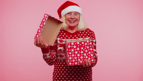 grandmother in christmas sweater smiling unwrapping gift opening box with pet cat great surprise