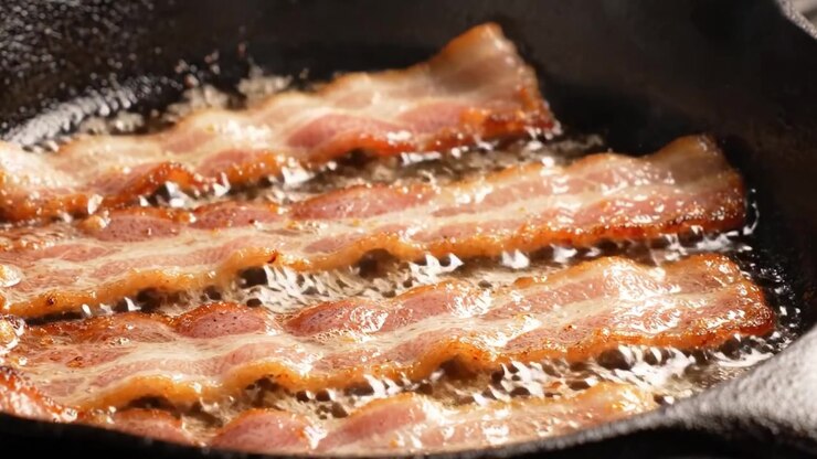 Pancetta sfrigolante in una padella di ghisa: una delizia culinaria di strisce croccanti e saporite che cuociono alla perfezione nel grasso caldo.