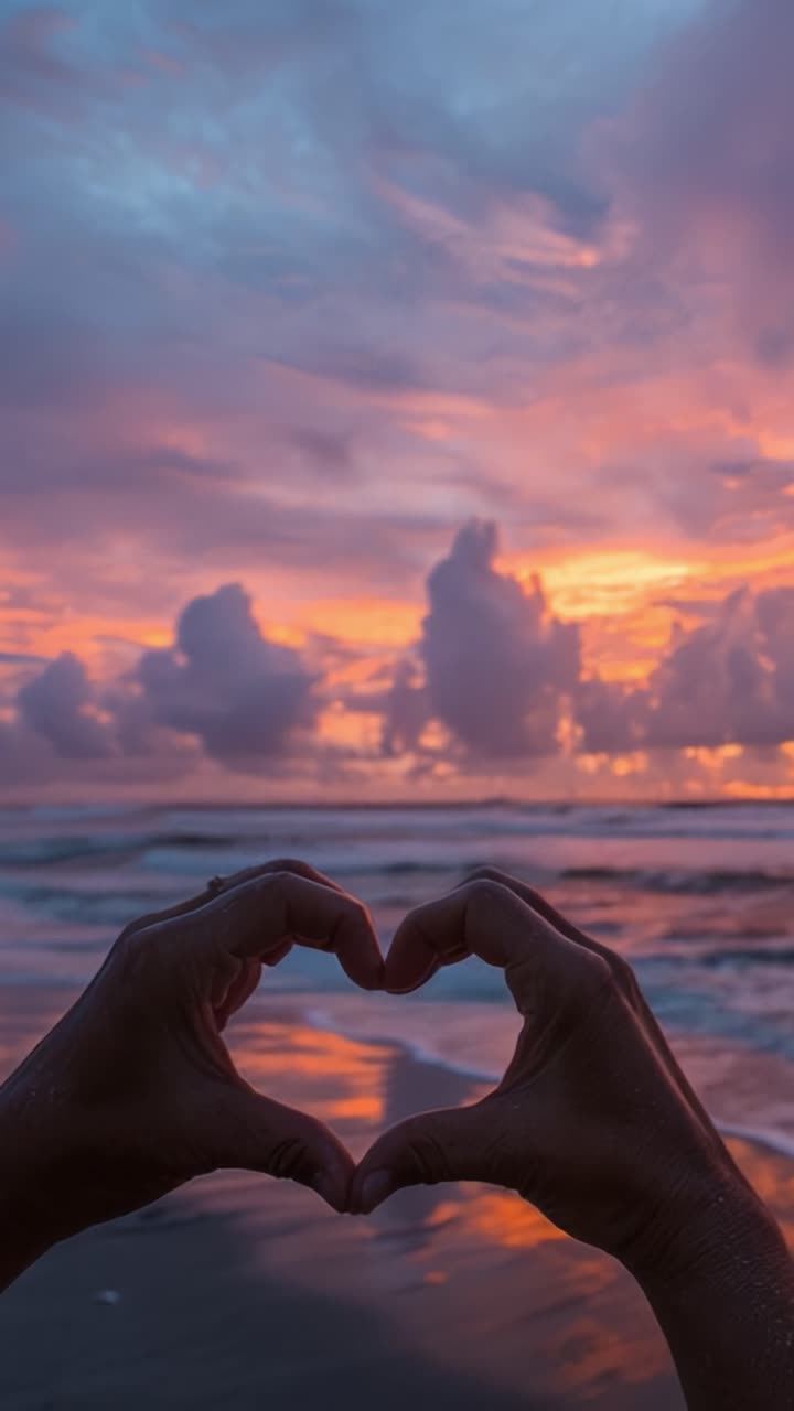 Un Sereno Tramonto sulla Spiaggia Che Cattura un Gesto a Forma di Cuore con le Mani Incorniciate Contro un Cielo Colorato, Emanando Amore e Tranquillità tra le Onde dell'Oceano