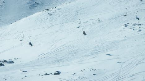 Chairlifts-of-alpine-ski-resort-transport-skiers-along-snowy-slope