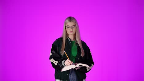 Beautiful-blonde-female-student-taking-notes-and-writing-in-book,-studio-shot