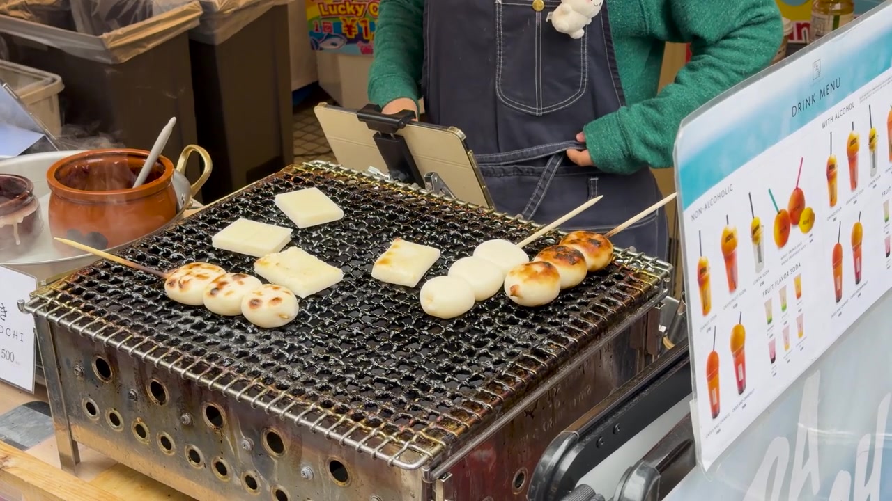 Seorang penjual memanggang kue beras dan sate dango di atas panggangan arang di Tokyo
